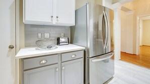Una cocina con armarios blancos, un refrigerador de acero inoxidable, un tostador y un cuenco de vidrio sobre la encimera.