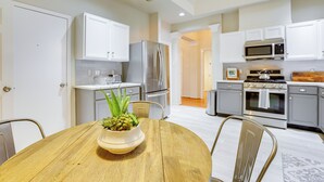 Una cocina moderna con gabinetes blancos, electrodomésticos de acero inoxidable y una mesa de comedor de madera con un centro de mesa.