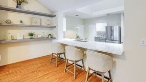 Una cocina moderna con encimera blanca, electrodomésticos de acero inoxidable y suelo de madera.