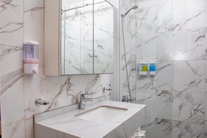 A bathroom with a marble-tiled wall, a sink with a mirror, a handheld showerhead, and a soap dispenser. - Venue 360 (Freetown)