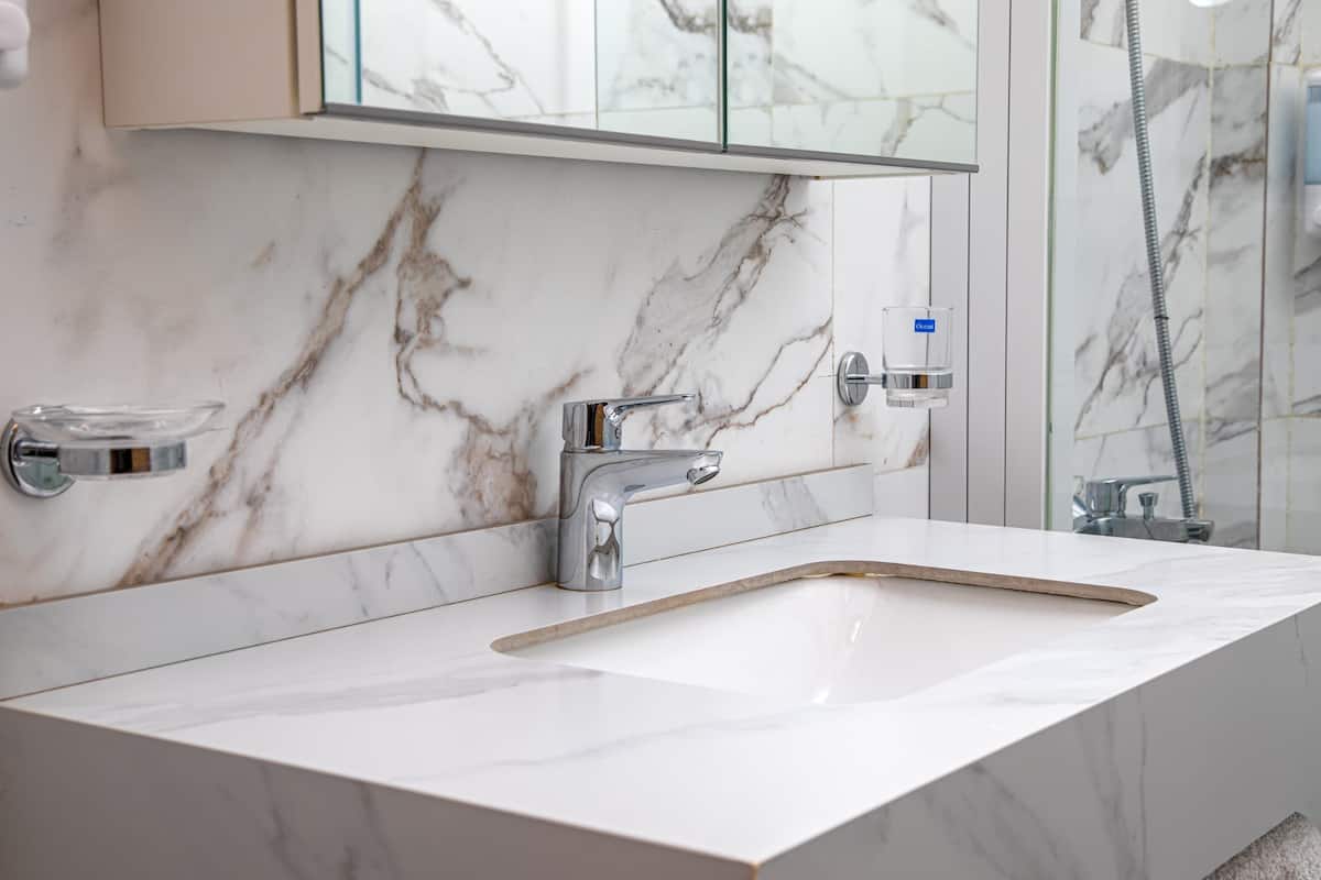 A bathroom with a marble sink, chrome faucet, and a glass soap dispenser.