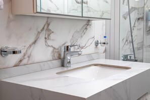 A bathroom with a marble sink, chrome faucet, and a glass soap dispenser. - Venue 360 (Freetown)