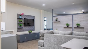 A modern living room with a grey sofa, a flat-screen TV mounted on a marble wall, and a small table with a chair. - Venue 360 (Freetown)