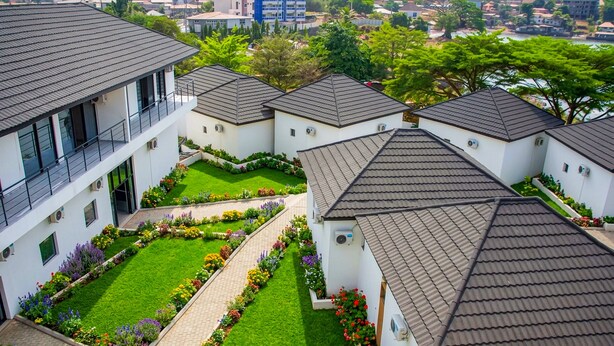 A modern building with multiple units, a central courtyard with a lawn and flower beds, and a view of surrounding residential area. - Venue 360 (Freetown)