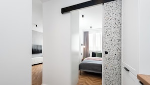 A modern bedroom with a herringbone-patterned floor, a bed with a grey and white duvet, and a wall with a speckled backsplash. - Szafir - by Kairos Apartments (Gliwice)