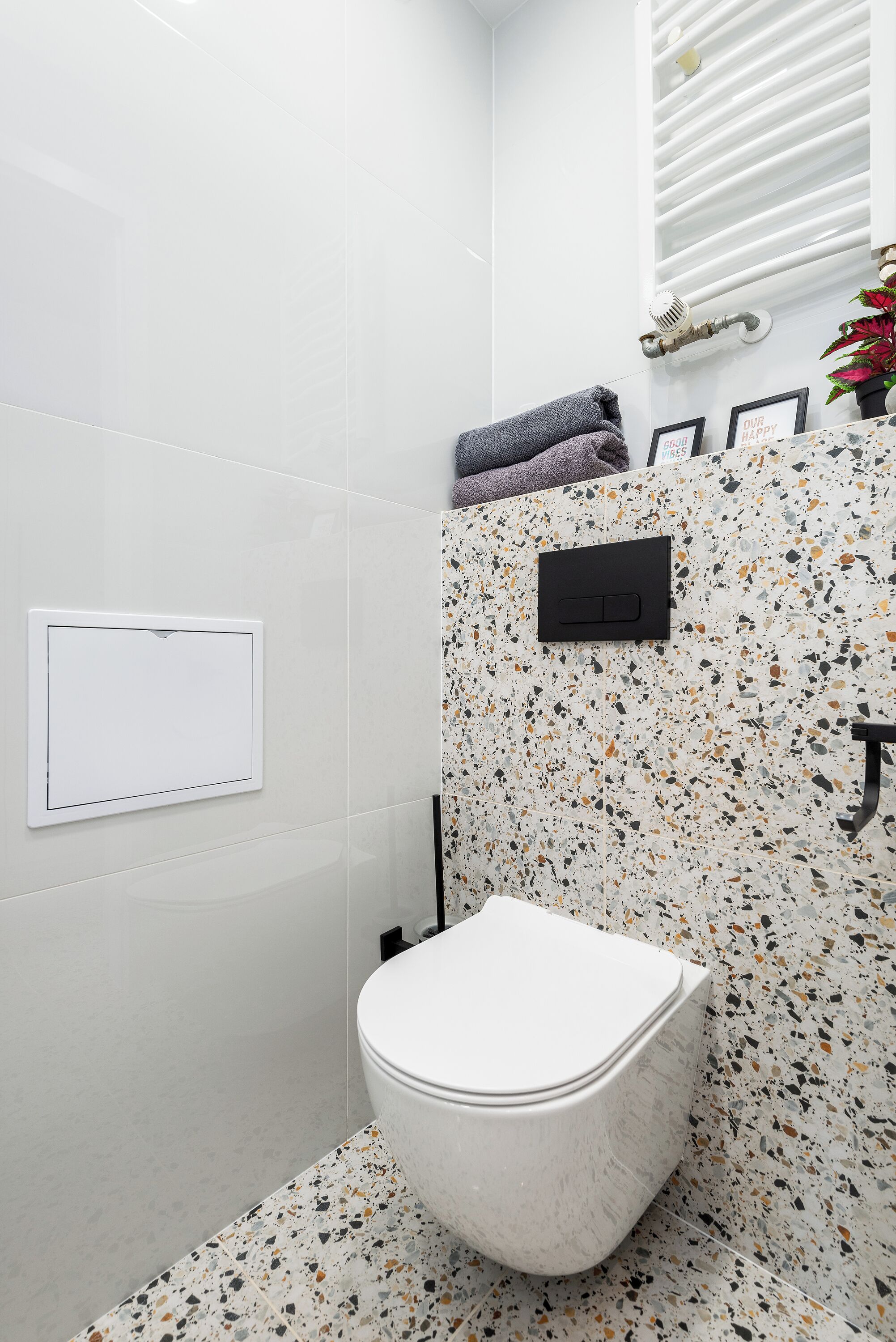 A bathroom with a white toilet, a shower with a white wall, and a speckled tile backsplash.