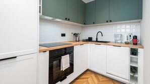 A modern kitchen with white cabinets, a black oven, a wooden countertop, and a green backsplash. - Szafir - by Kairos Apartments (Gliwice)