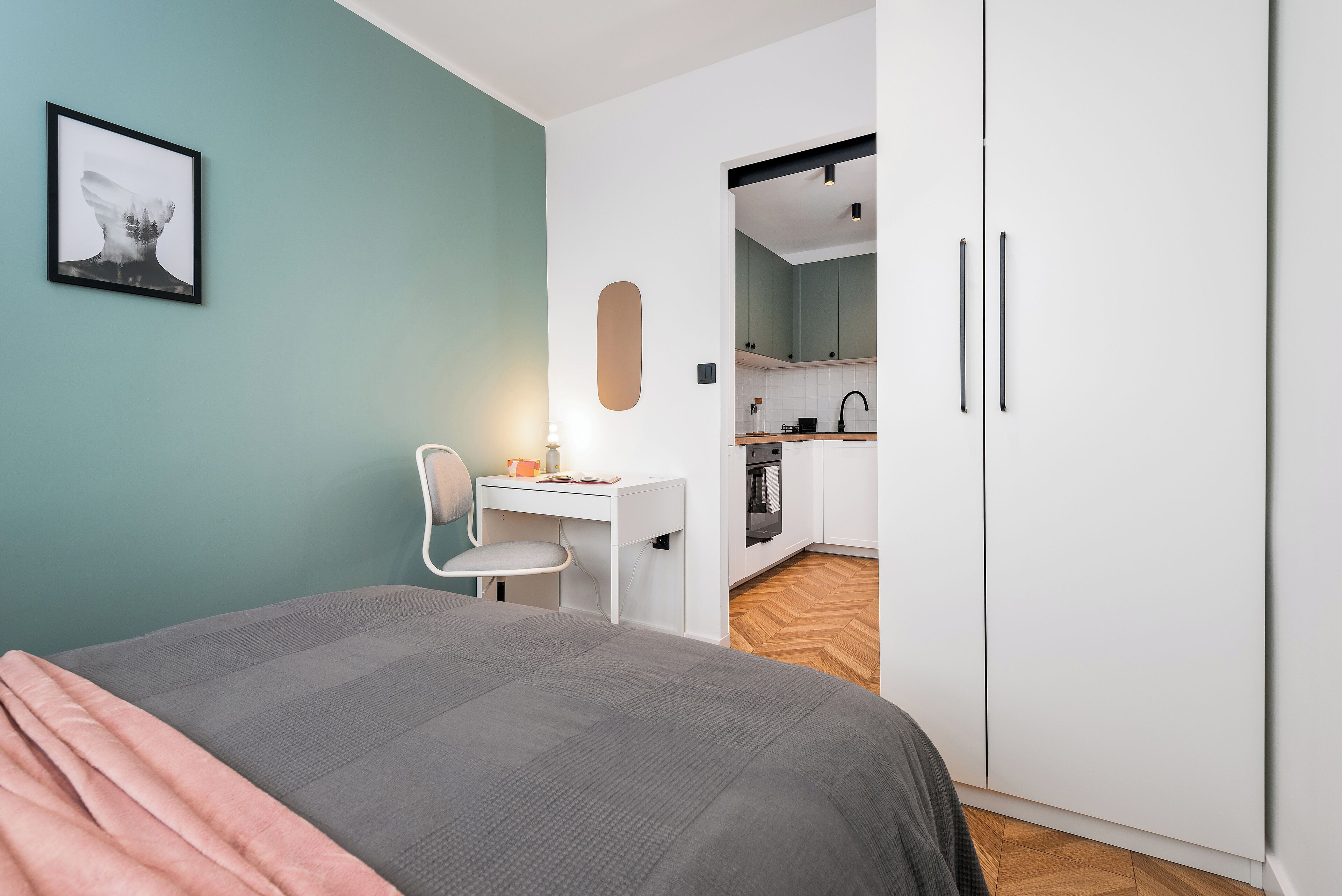 A bedroom with a bed, a desk, and a kitchenette.