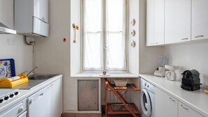 Eine kompakte Küche mit Backofen, Geschirrspüler, Waschmaschine und einem Fenster mit Vorhängen.