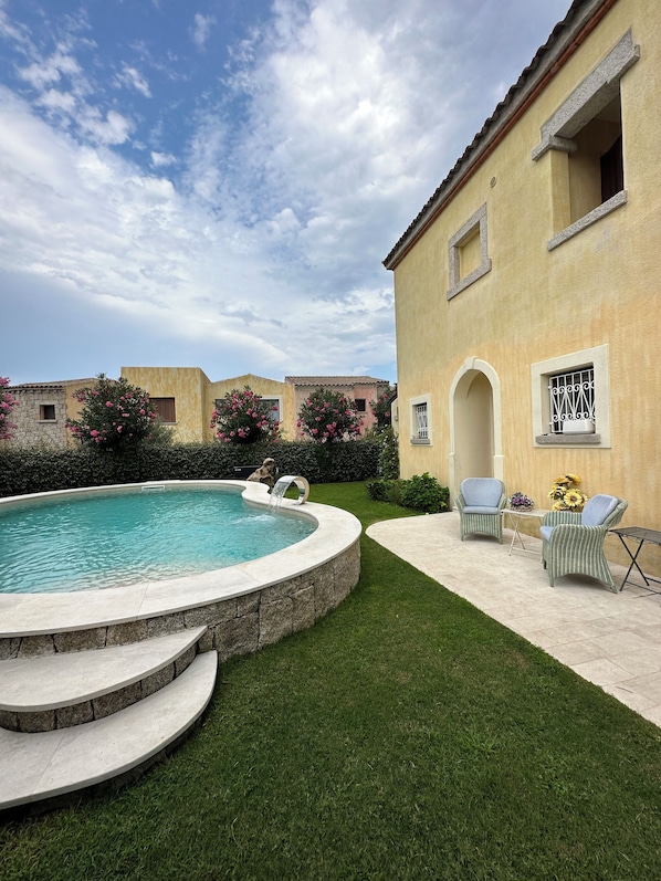 A pool area with a circular pool, steps leading into the water, and two wicker chairs with a small table and sunflowers.