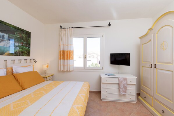 A bedroom with a bed, a nightstand, a TV, a wardrobe, and a window with curtains.