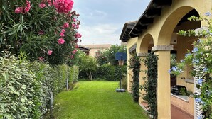 Un jardín bien cuidado con césped, plantas en flor y un edificio con arcos y techo de tejas.