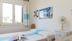 Un dormitorio con cama, una mesita de noche con lámpara, un cuadro enmarcado en la pared y una ventana con cortinas.