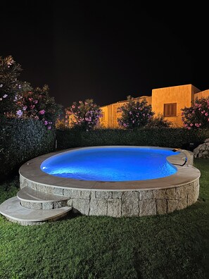 Una piscina con borde de piedra, rodeada de césped cuidado y arbustos florecientes.