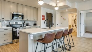 A modern kitchen with a central island, stainless steel appliances, and bar stools.