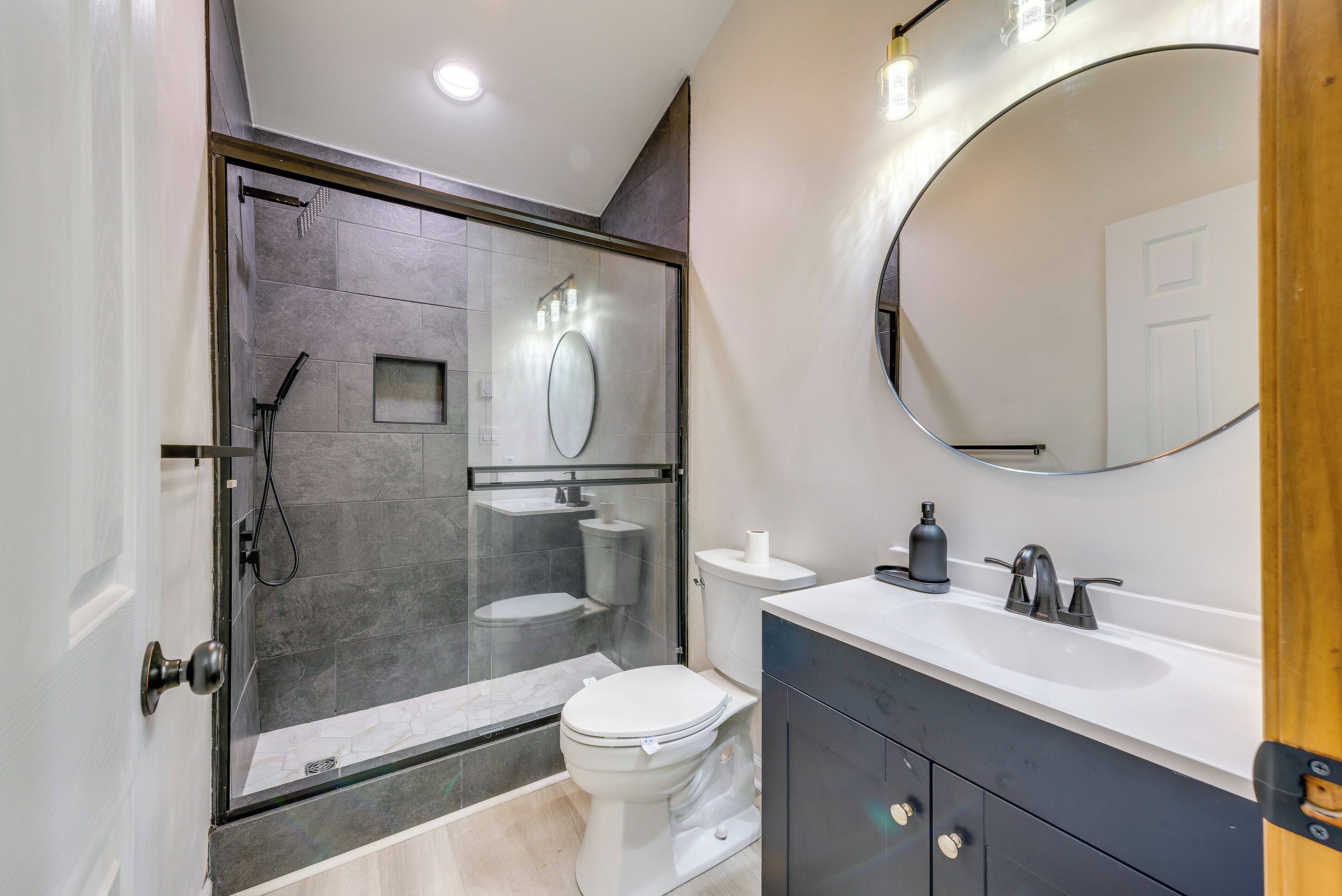 A modern bathroom with a glass-enclosed shower, a white toilet, a large mirror, and a dark vanity with a sink.