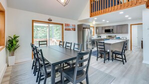 A spacious dining area with a large table and chairs, a kitchen with modern appliances, and a wooden staircase. - Lakefront Poconos Cabin w/ Deck & Game Room (Blakeslee)