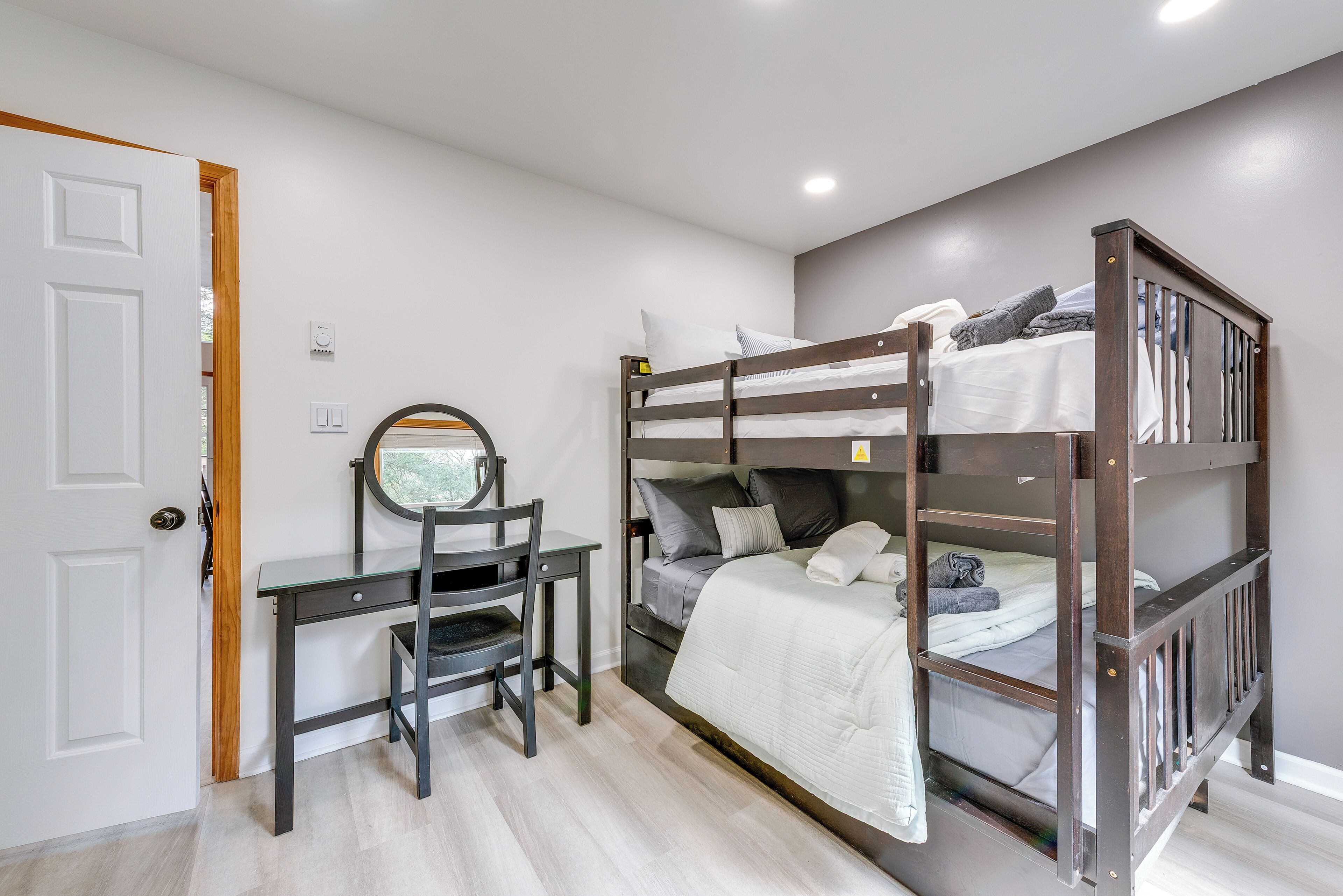 A bunk bed with a desk and chair, a door, and a light switch on the wall.