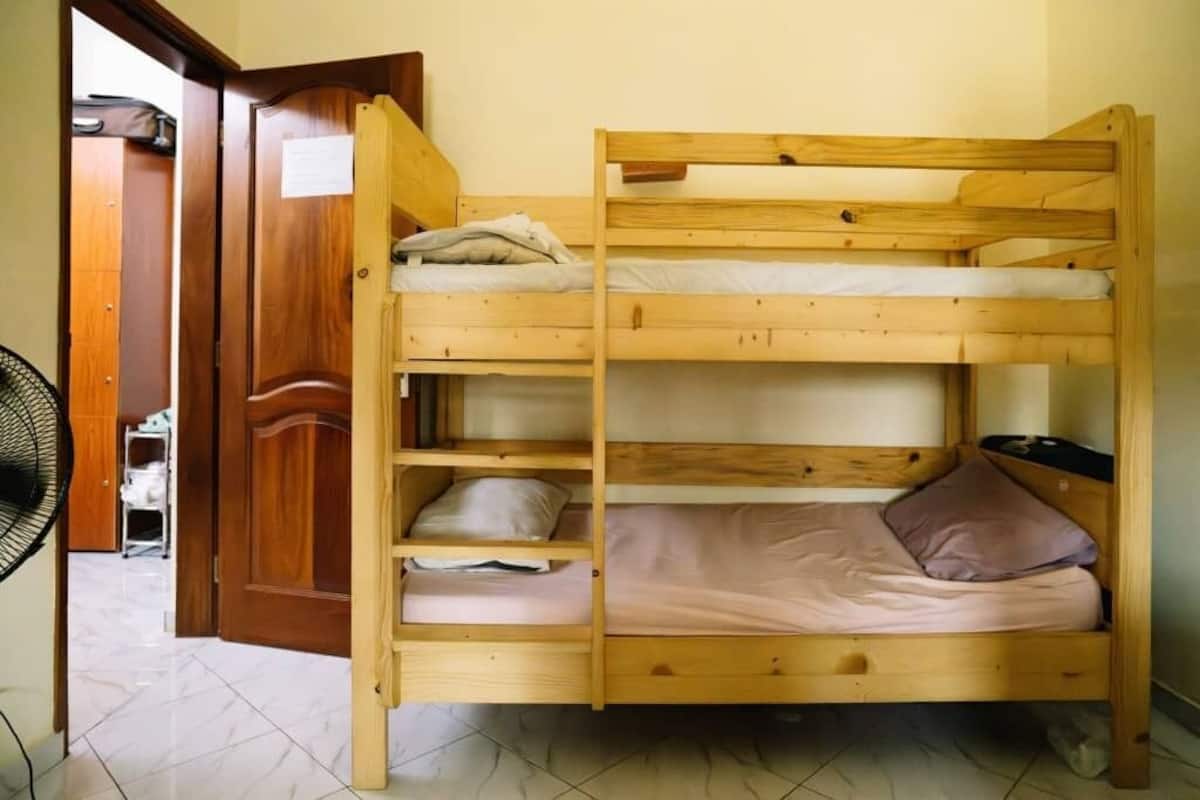 Un lit superposé à deux niveaux, une porte en bois et un ventilateur dans la pièce.