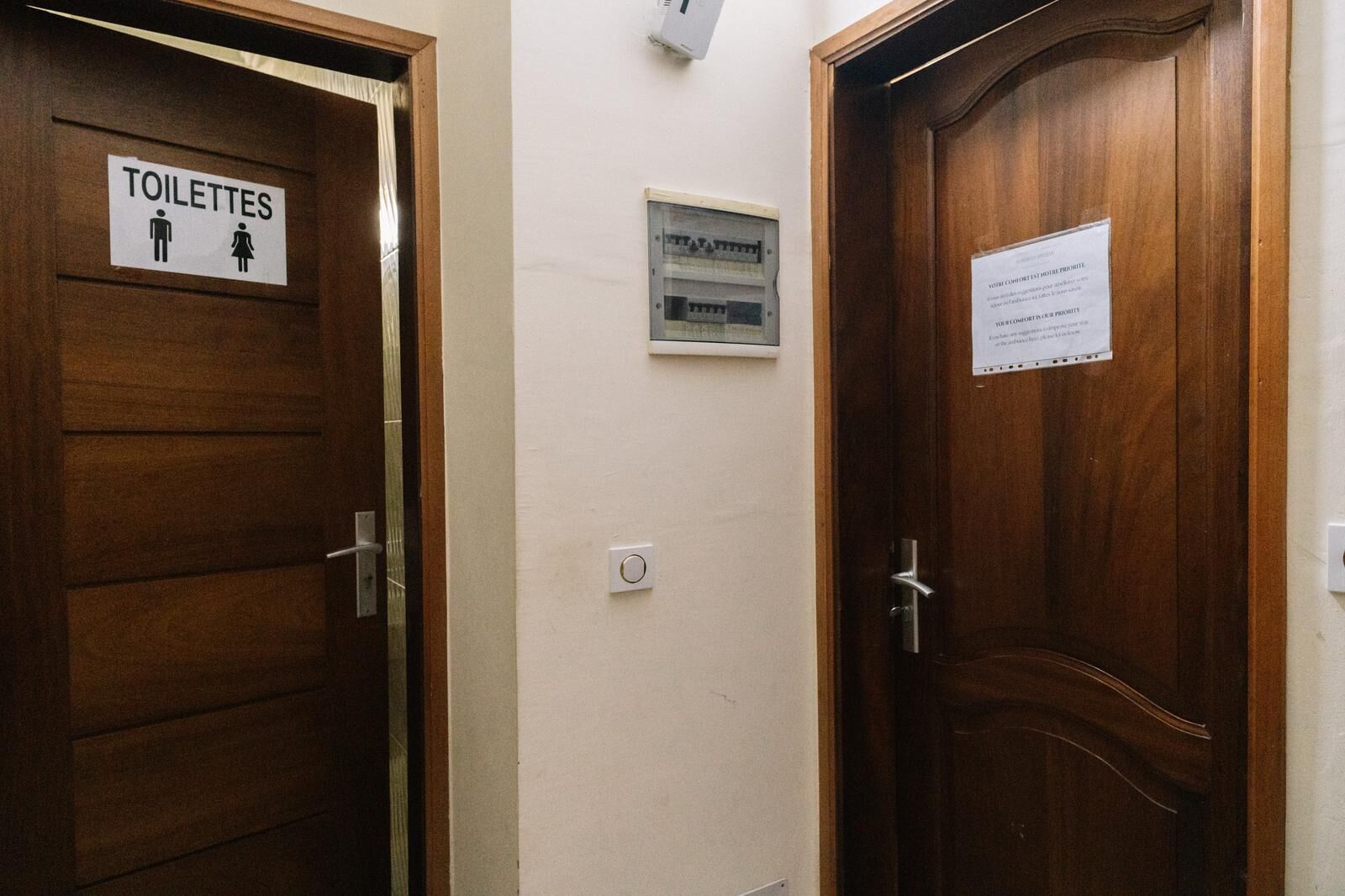 A hallway with wooden doors, one labeled 'TOILETTES' with male and female symbols, and another with a sign about voting.