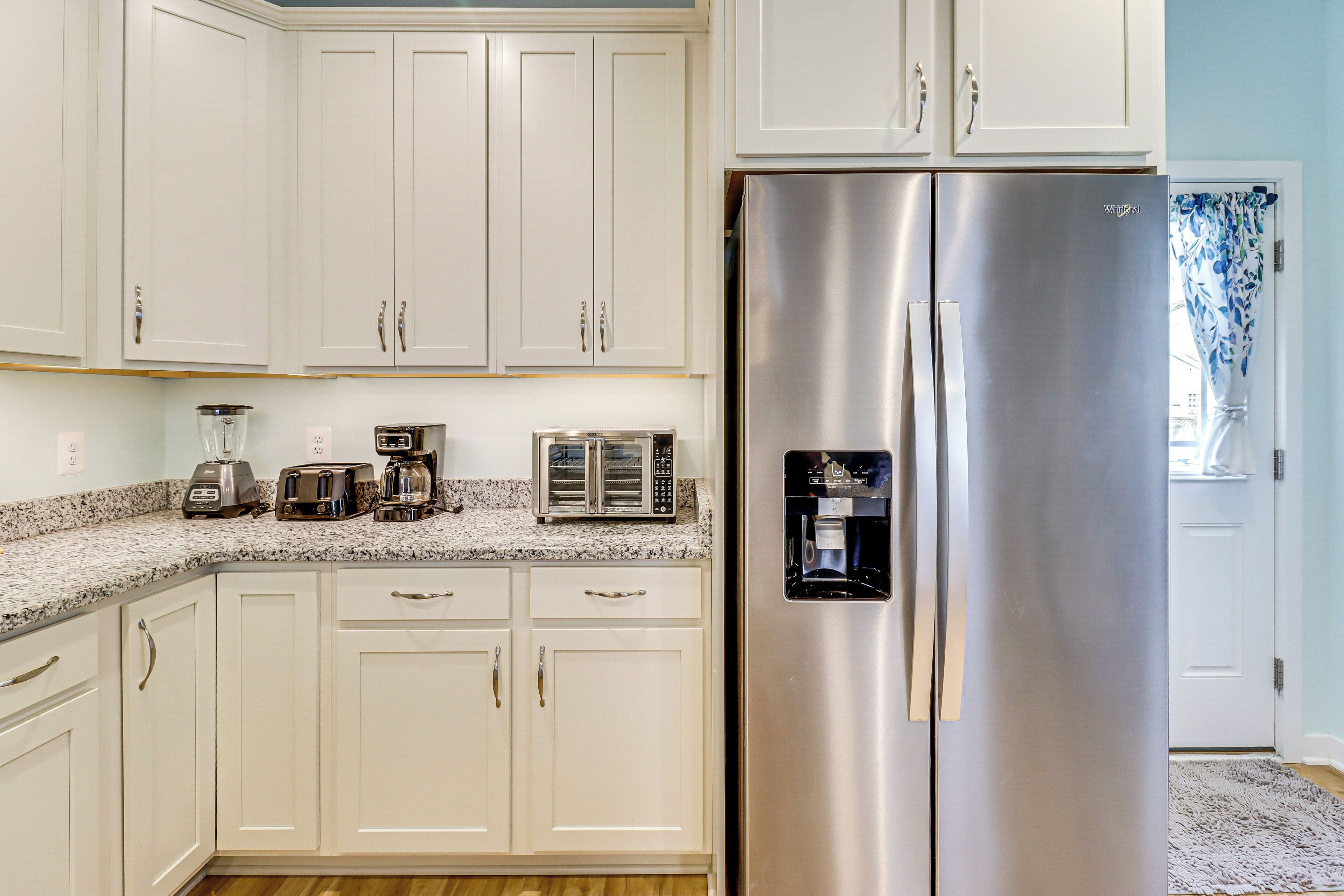 A kitchen with white cabinets, a stainless steel refrigerator, a coffee maker, and a toaster.