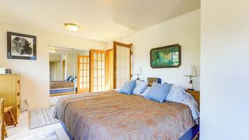 A bedroom with a large bed, a wooden wardrobe, a mirror, and a painting on the wall.