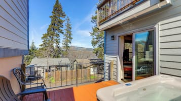 A balcony with a hot tub, wooden deck, and a view of a backyard with trees and a distant mountain.