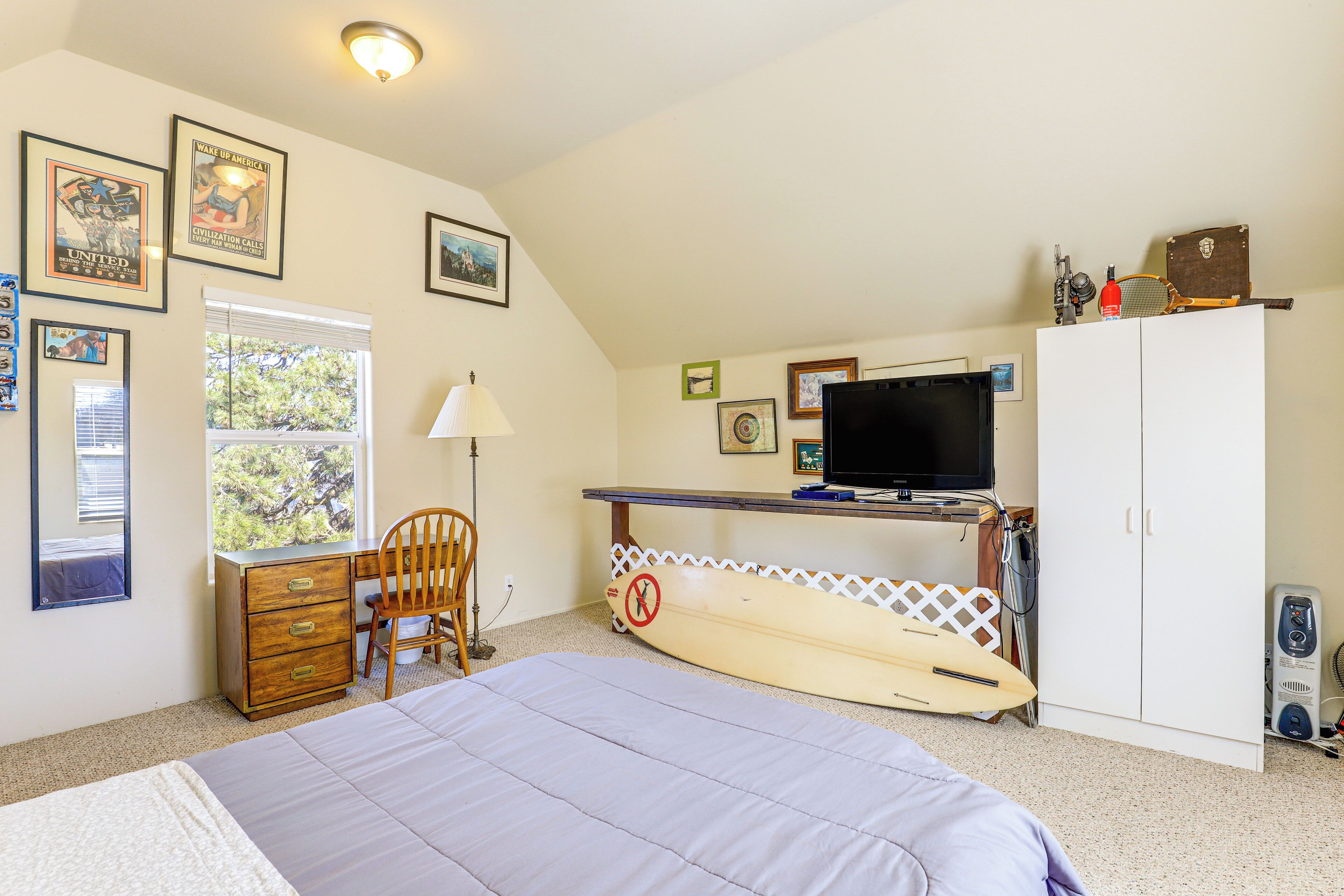 Un dormitorio con cama, escritorio, computadora, tabla de surf y televisor.