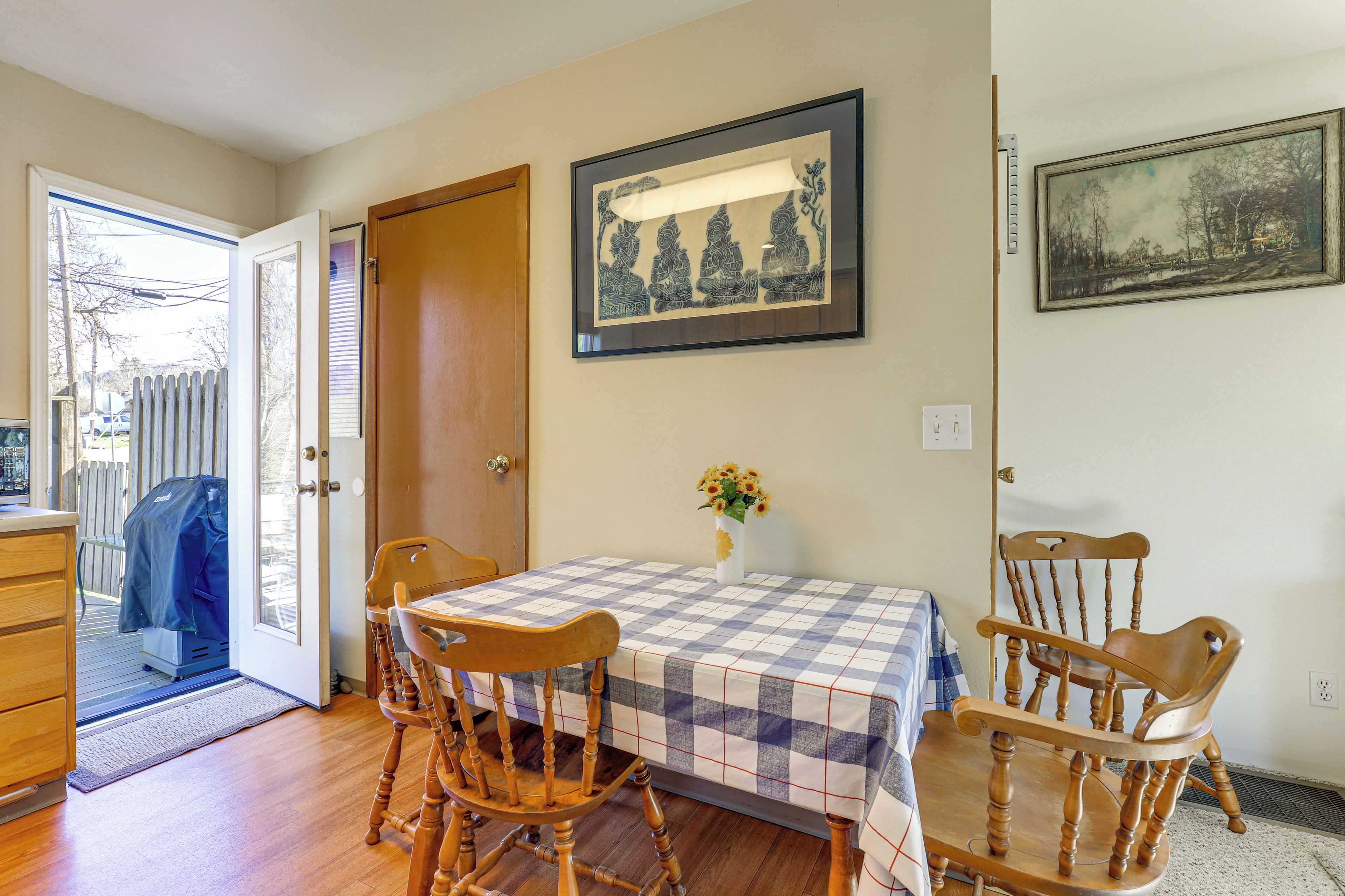 A dining area with a checkered tablecloth, wooden chairs, a vase with flowers, and framed artwork on the walls.