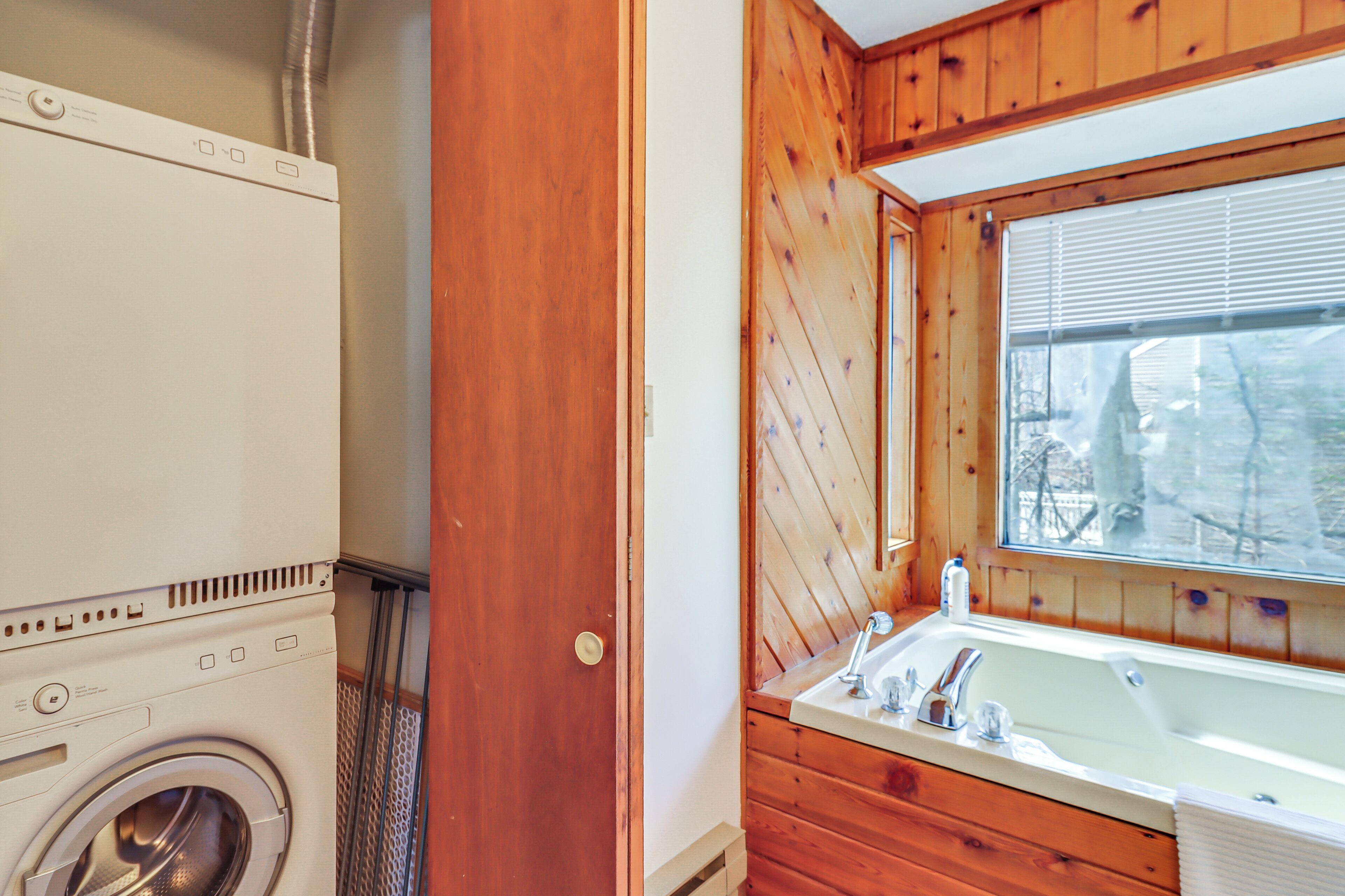 A compact bathroom with a washing machine, wooden walls, a sink, and a window.