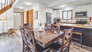 A modern kitchen with white cabinets, stainless steel appliances, and a wooden dining table with chairs. - 3 Mi to Tobyhanna State Park: Home w/ Serene Deck! (Tobyhanna)
