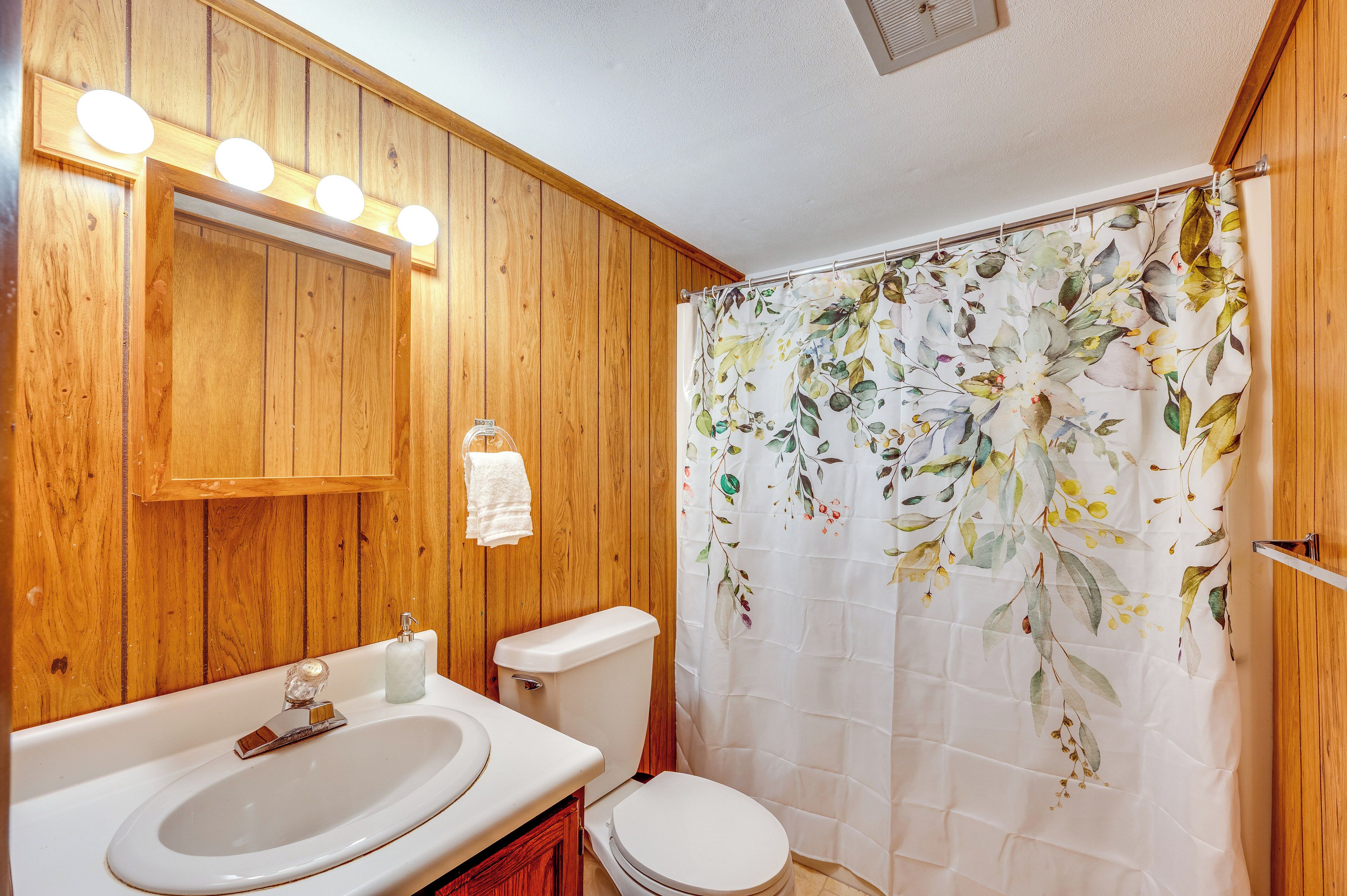 Un baño con paredes de madera, un lavamanos blanco, un inodoro y una cortina de ducha con estampado floral.
