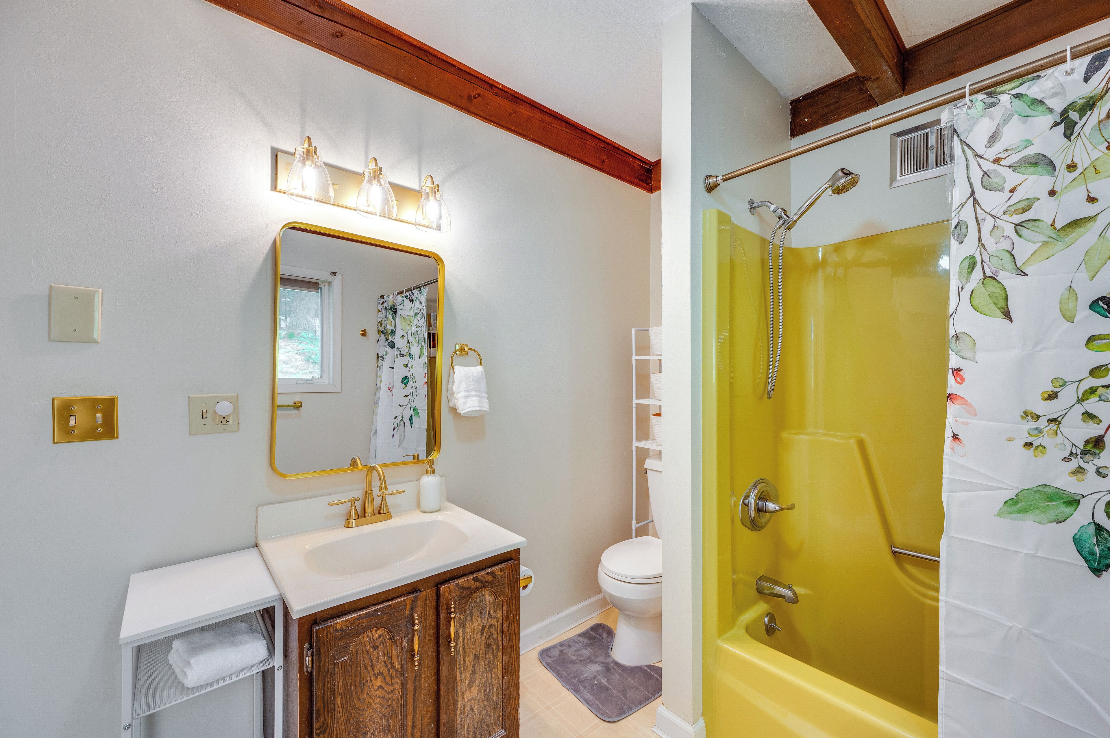 Un baño con lavamanos blanco, tocador de madera, espejo con luces, inodoro y bañera amarilla con cortina de ducha.