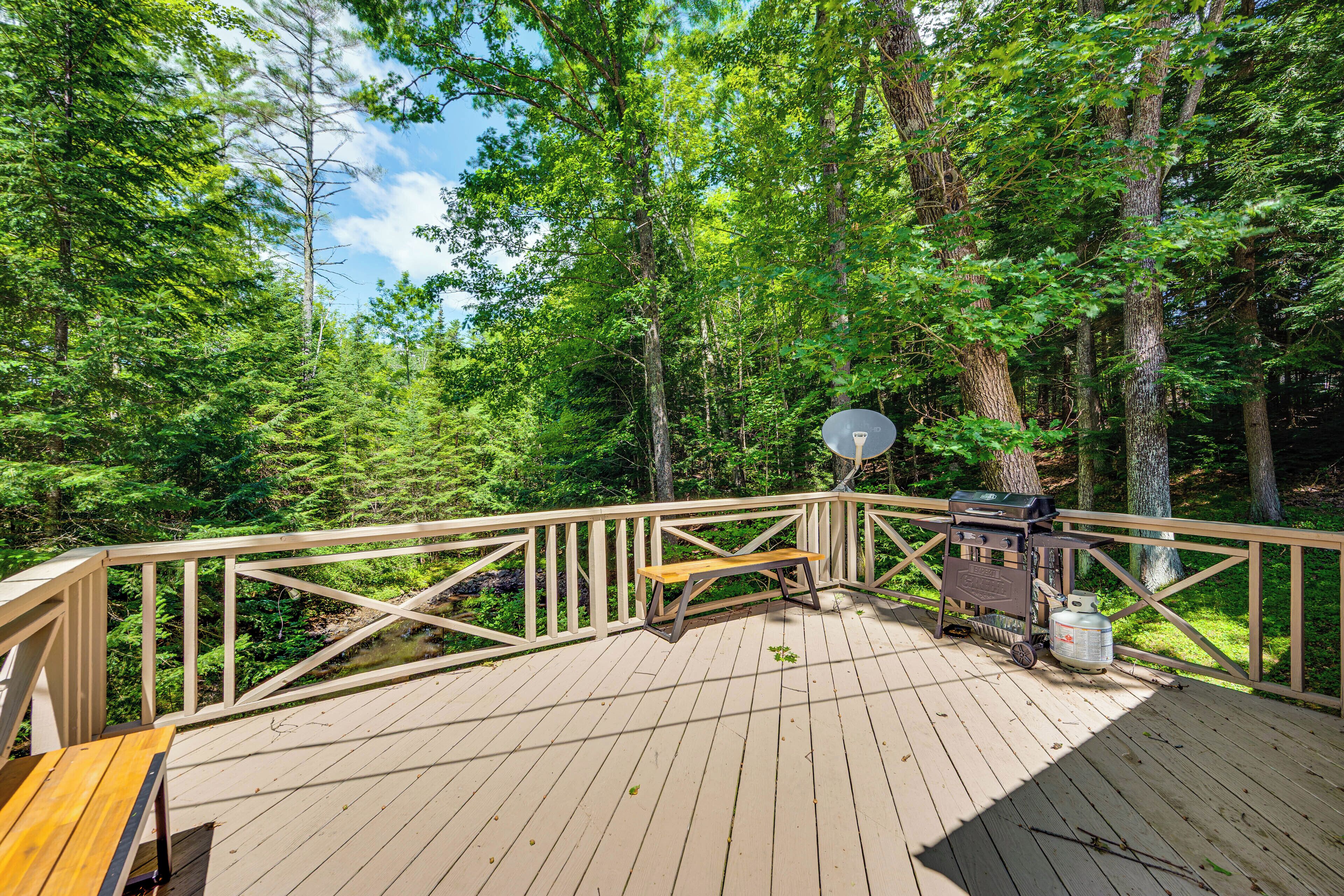 A wooden deck with a picnic table and grill, surrounded by a forest.