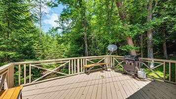 A wooden deck with a picnic table and grill, surrounded by a forest.