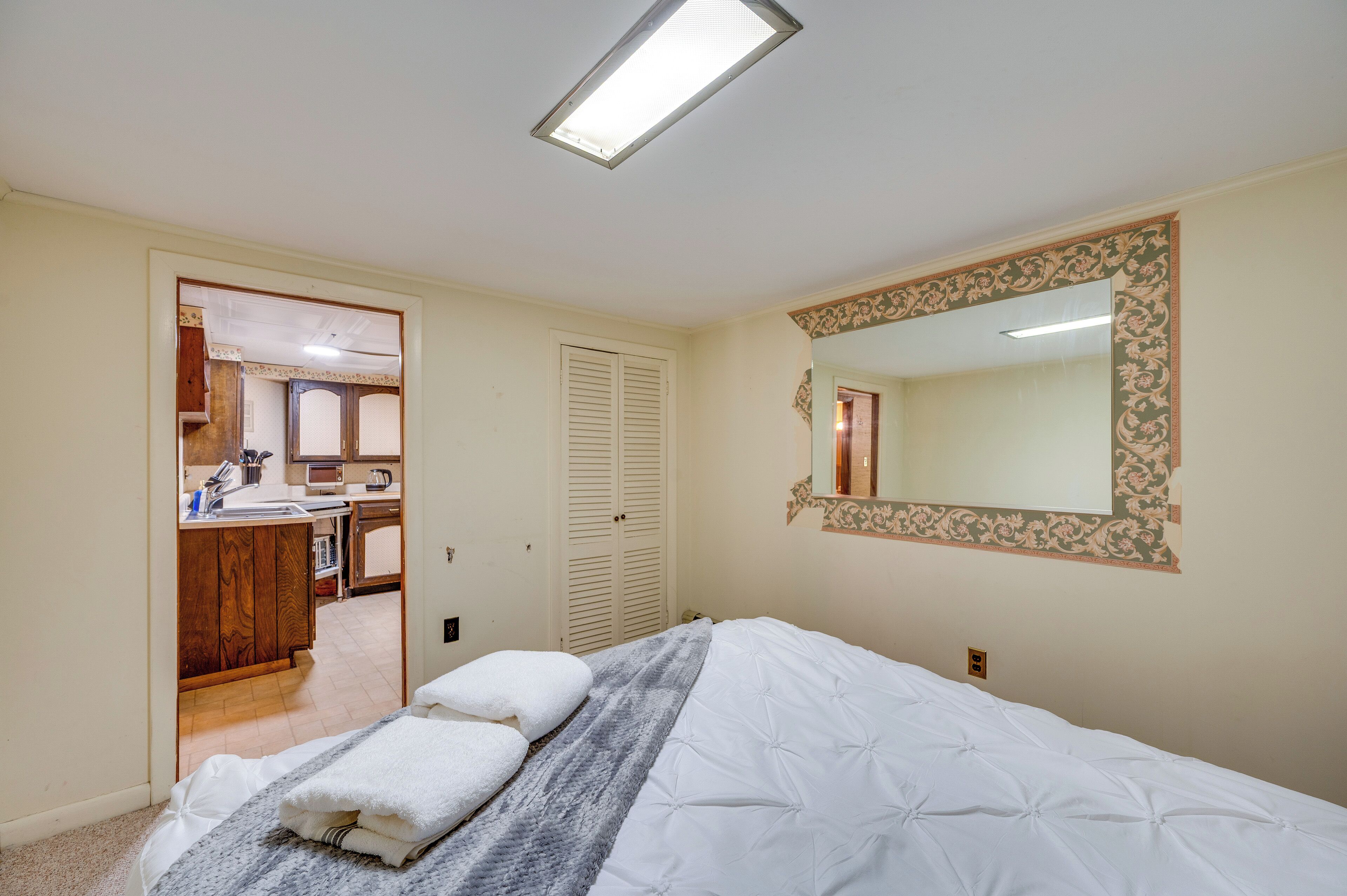 Een slaapkamer met een bed, nachtkastje, spiegel en een deur naar een badkamer.