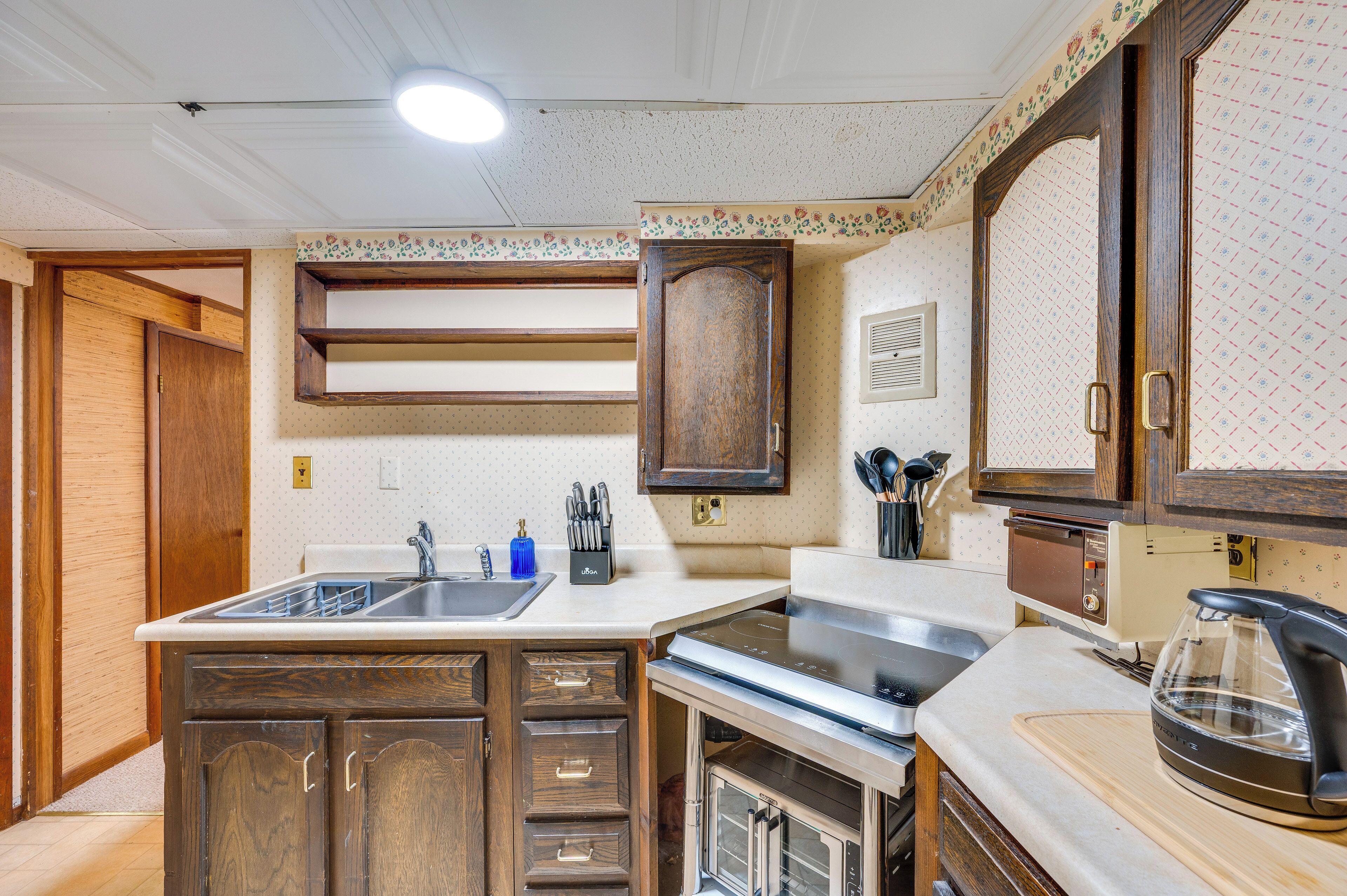A kitchen with wooden cabinets, a sink, a stove, and a kettle.