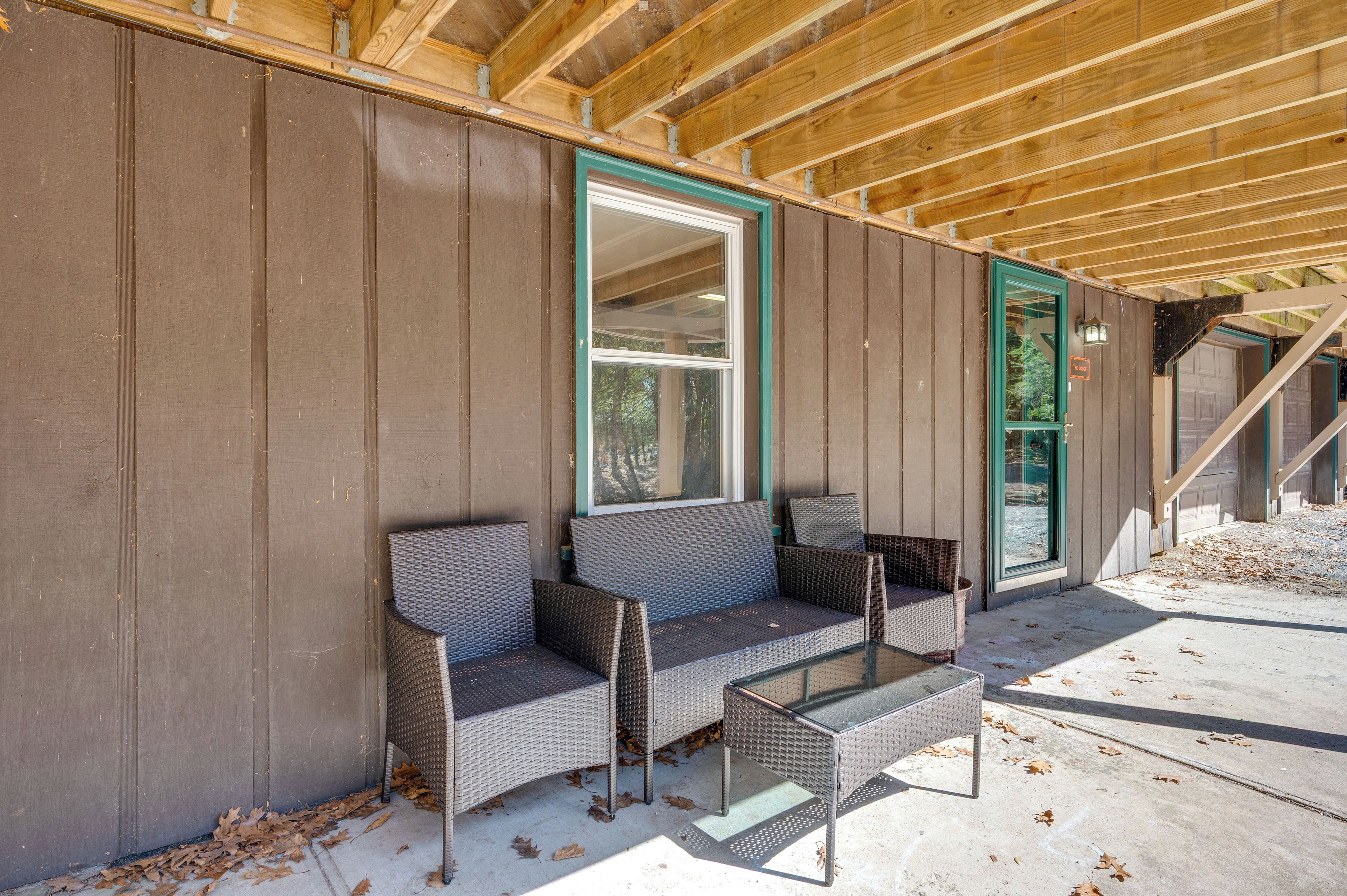 A covered outdoor seating area with a sofa and chairs, a glass table, and a wooden ceiling structure.