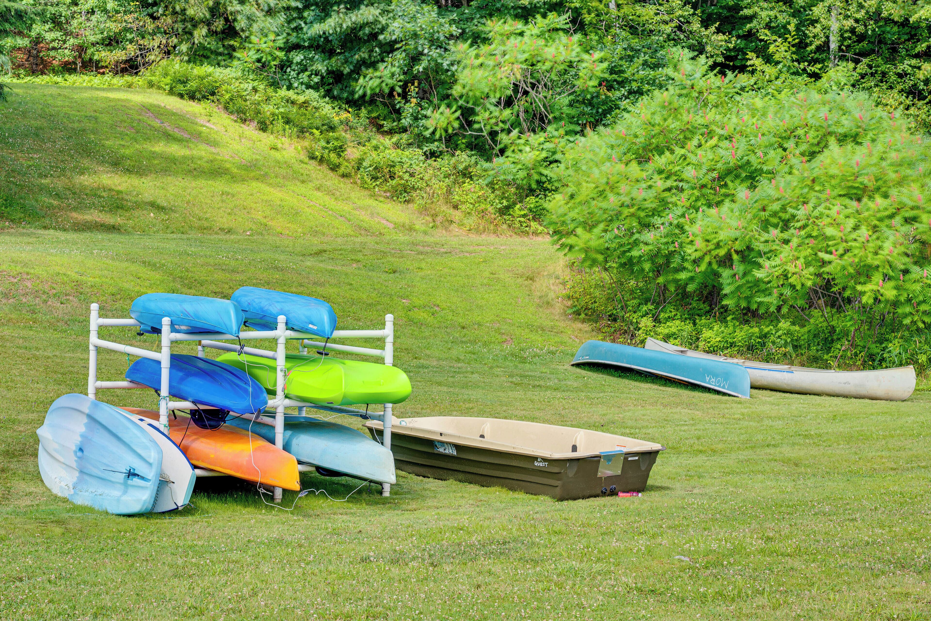 A grassy area with a white metal rack holding several kayaks and a canoe.