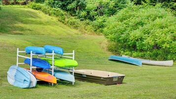 A grassy area with a white metal rack holding several kayaks and a canoe.