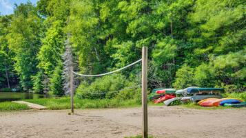 A sandy beach with a rope barrier, a wooden post, and several colorful kayaks and canoes.
