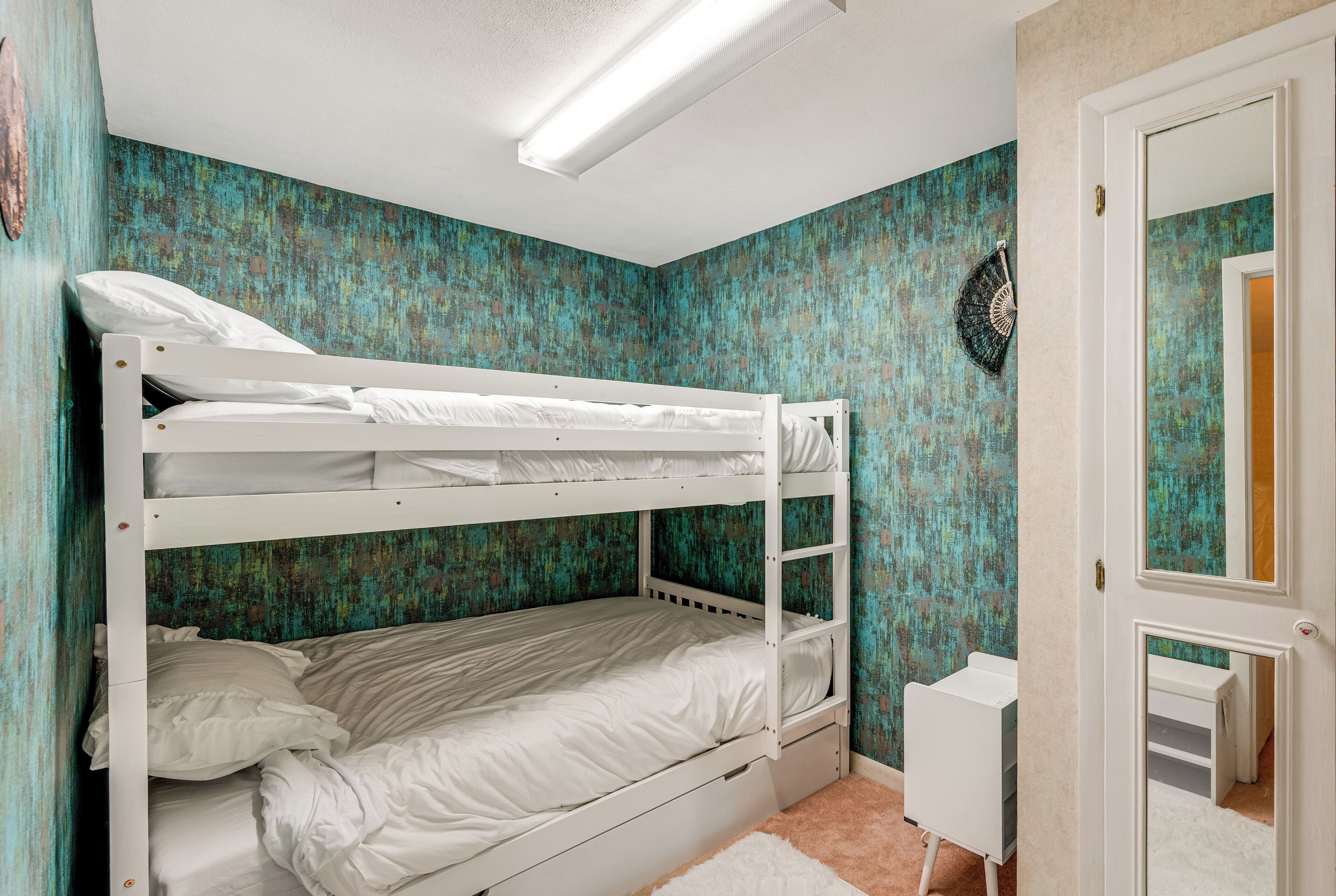 A bunk bed room with a teal textured wall, a white door, and a small white desk.