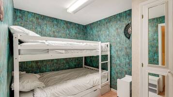 A bunk bed room with a teal textured wall, a white door, and a small white desk.