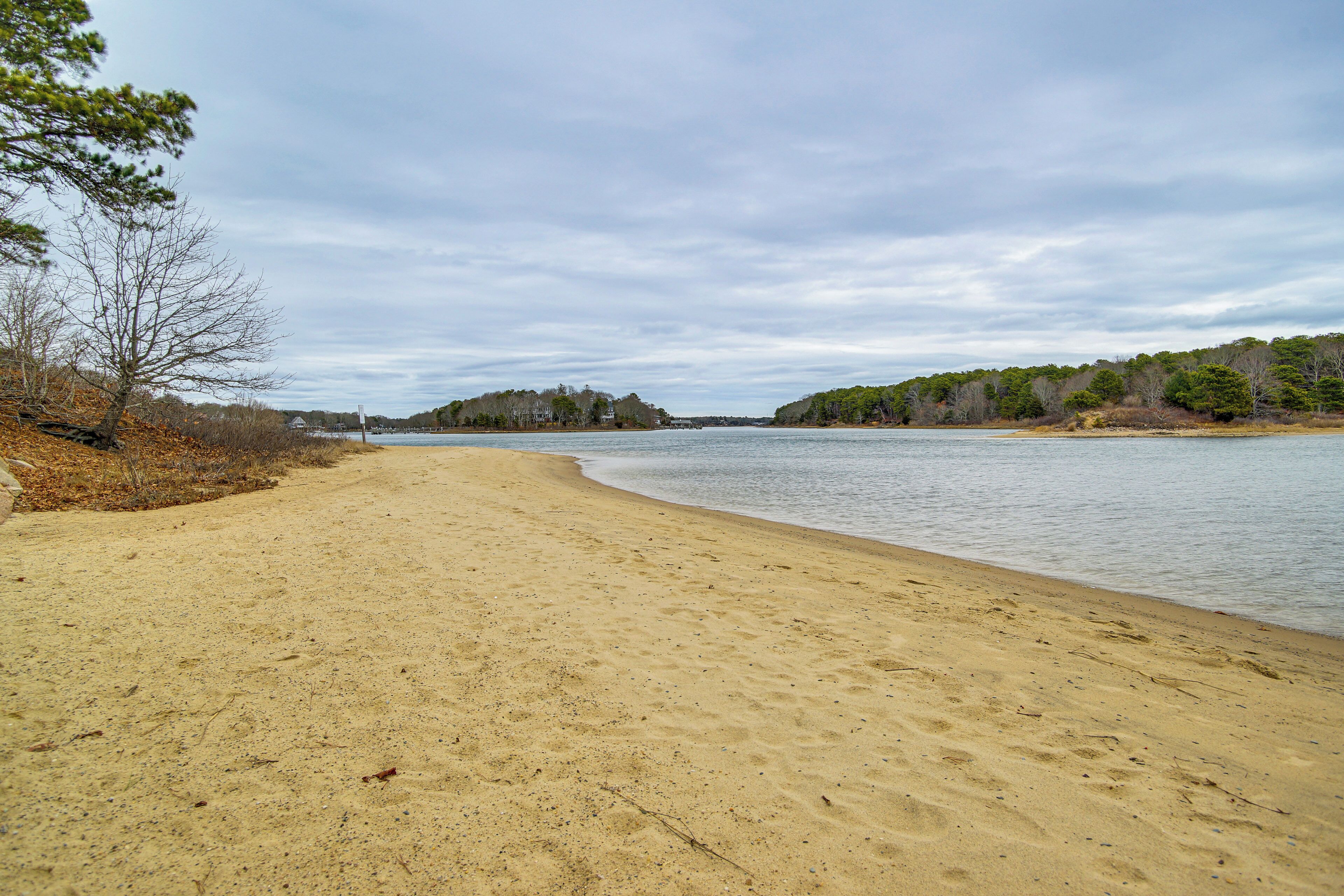 A sandy beach with a calm river, trees, and a distant shoreline.