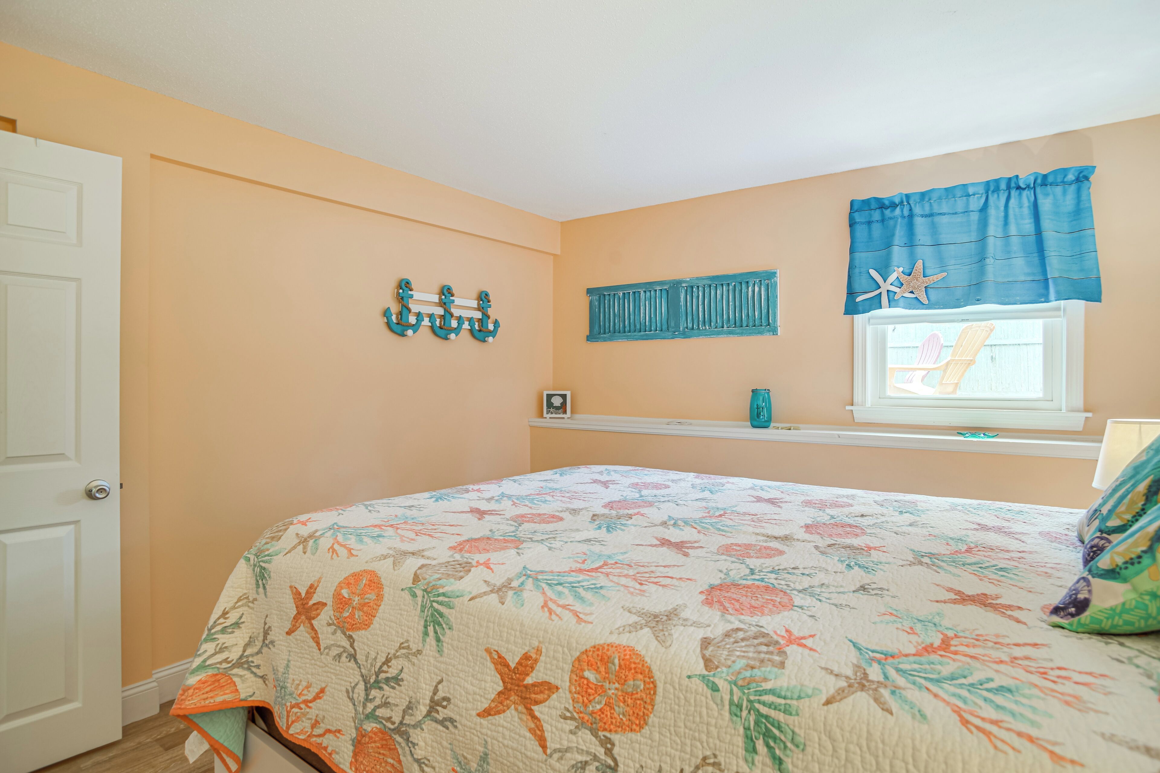 A bedroom with a floral bedspread, a window with a blue valance, and nautical-themed wall decor.