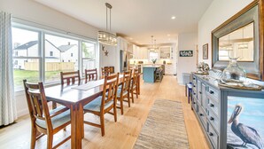 A spacious kitchen with wooden cabinets, a dining area with a large table and chairs, and a view of the backyard through large windows. - Walk to Beach & Central Park: Home in Cape Charles (Cape Charles)