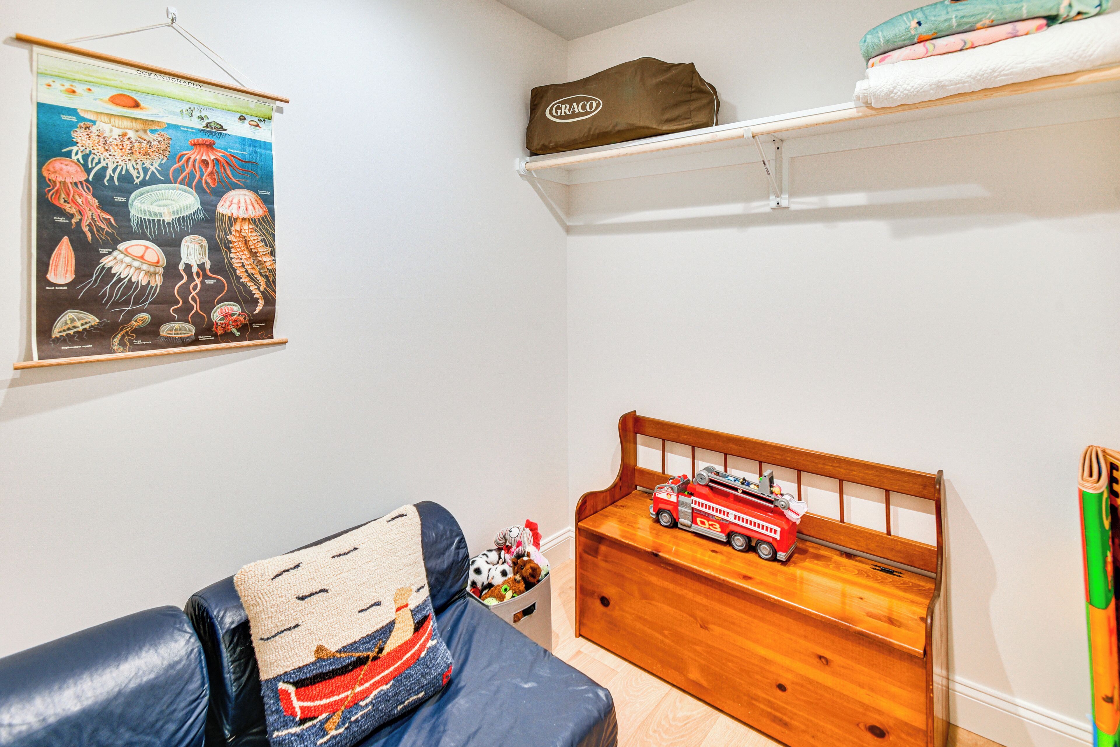 Una habitación infantil con una cama, una mesita de noche de madera, un estante con un saco Graco y un cartel de medusas.