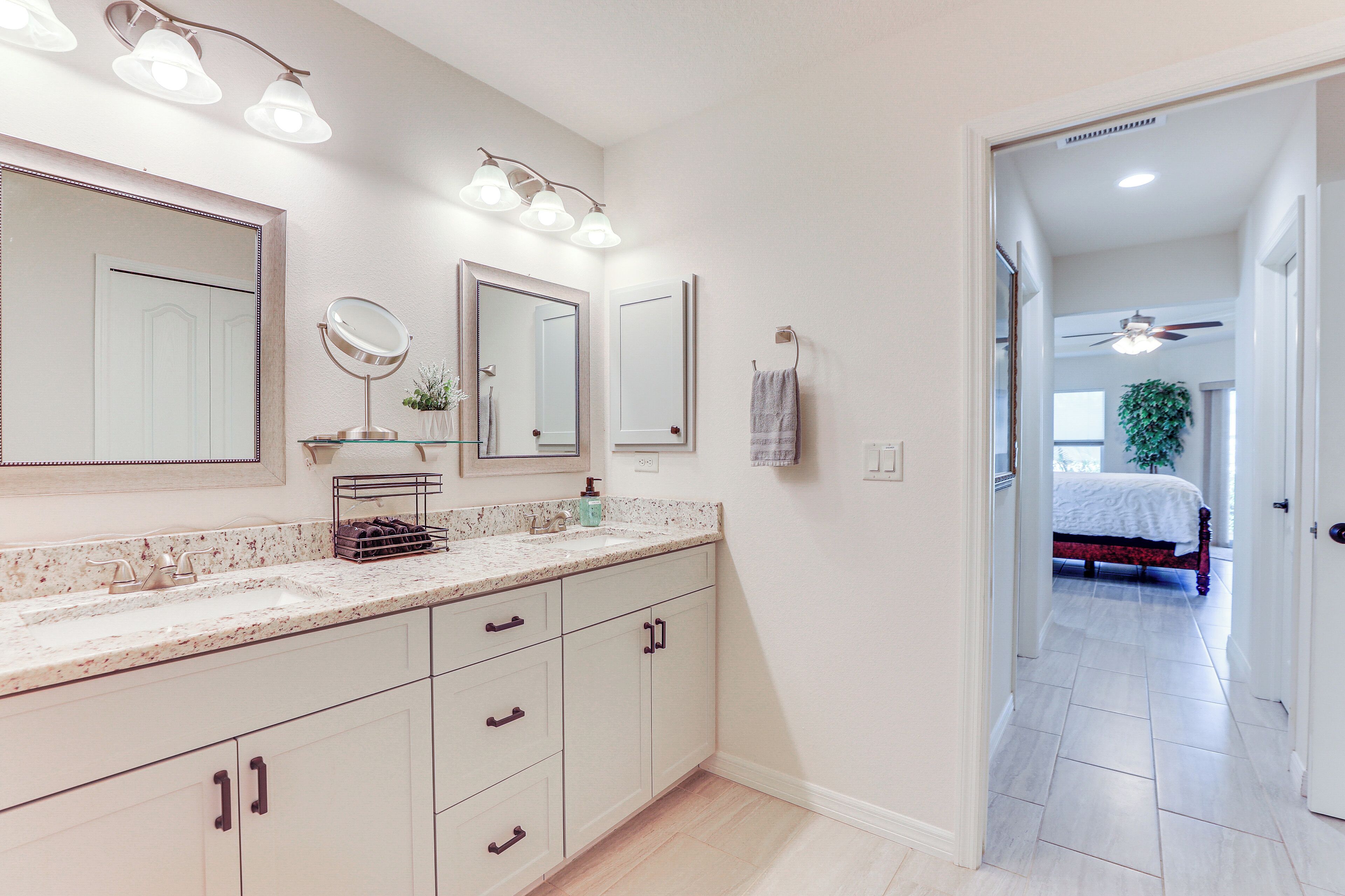 A bathroom with a large mirror, a sink, and a vanity with drawers. There is a towel hanging on the wall and a plant on the counter.