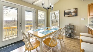 A dining area with a wooden table, white chairs, and a chandelier. There are large windows with a view of the outdoors. - Water-view Deck: Home on Dale Hollow Lake (Albany)