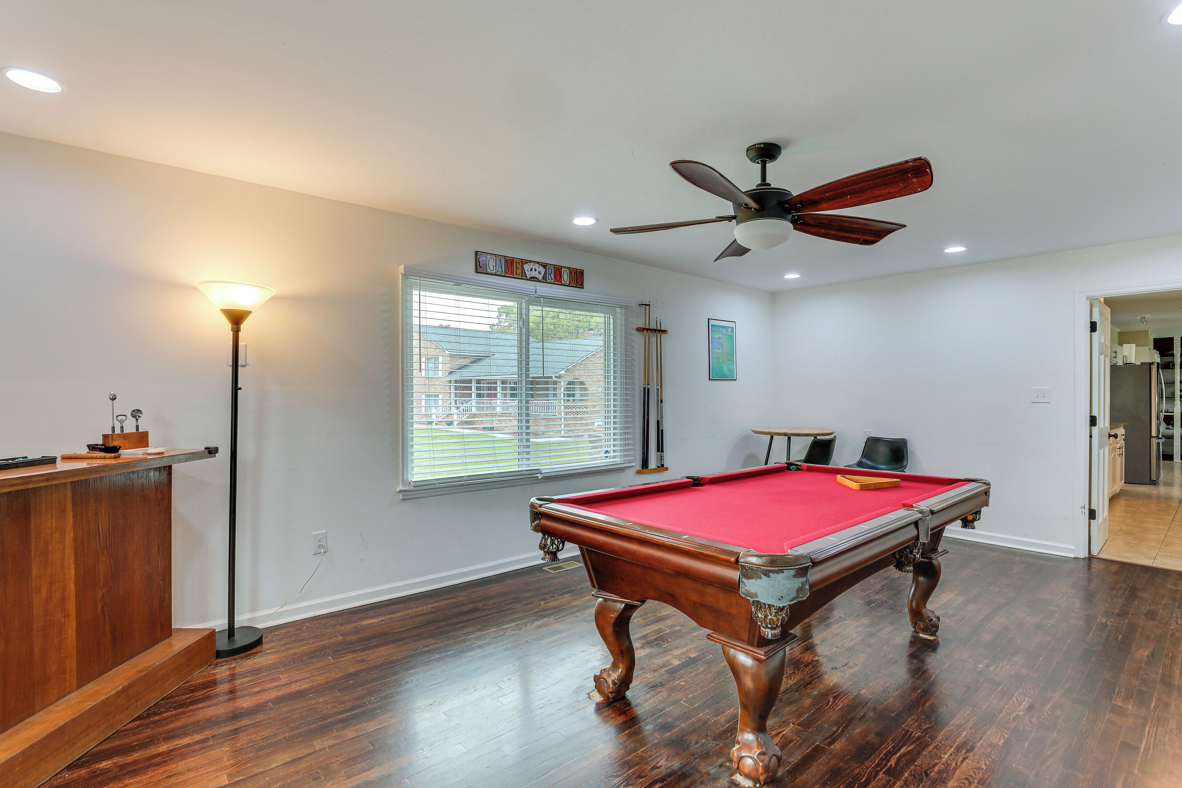A pool table with a red felt surface, a ceiling fan, and a window with blinds.
